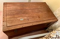 Top angled view of the wooden trunk showing the rectangular shape, plank design, and wood grain surface with a small label and key on top.