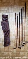 Full view of brown leather golf bag and six hickory shaft clubs laid on floor