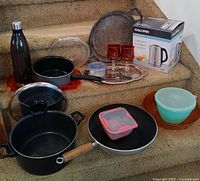 Overall view of entire lot on stairs, showing cookware, serving pieces, storage containers, water bottle and boxed kettle