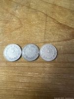 Reverse side of three 5 centavos coins showing denomination and wreath