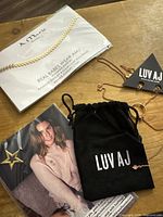 Group shot showing LUV AJ pouch, rose gold necklace, A. Marie carded necklace, promotional card