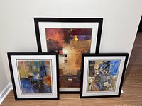 Front view of all three framed abstract art pieces leaning against wall