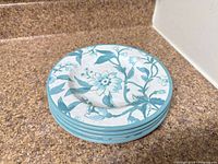 Stack of five teal floral plates on countertop