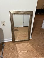 Rectangular beveled mirror with metallic patterned frame leaning against wall