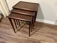 Three dark wood nesting tables stacked to show size progression, overall view