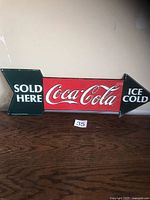 Front of embossed Coca-Cola arrow sign showing graphics and text
