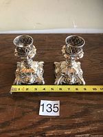 Two matching silver-plated candle holders on wooden surface with measuring tape showing height and lot number tag.
