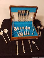 Open chest showing knives, forks, teaspoons and serving pieces, plus additional servers laid out