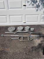 All weight plates and three bars laid out on driveway in front of garage door