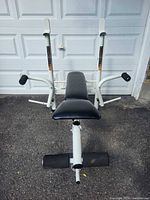 Front angle of white weight bench showing padded sections, barbell uprights, leg developer