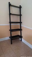Full front view of black 5-shelf ladder shelf in corner
