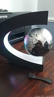 Globe levitating inside C-shaped LED frame on desk