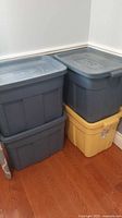 Four Rubbermaid storage totes stacked, showing two blue on top of yellow