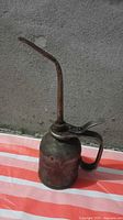 Front view of metal oil can showing bent spout, handle and lever
