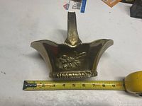 Front view of brass basket showing embossed floral motif and ruler indicating roughly 7 in length