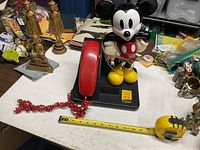 Full view of Mickey Mouse telephone with base, handset, cord, tape measure for scale