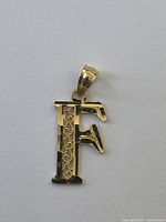 Front view of yellow gold letter F pendant showing filigree detail and bail