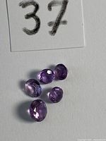 Five loose purple amethyst gemstones on white background under tag 37