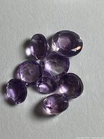 Seven loose light purple gemstones on white background