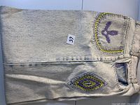 Full view of folded jeans showing embroidery on back pocket
