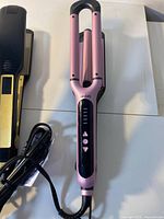 Pink triple-barrel curling iron and part of flat iron cord visible