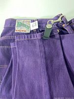 Front view showing purple jeans folded, Request Worldwide patch and size label