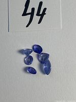 Five faceted tanzanite gemstones on white background with lot number