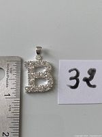Front view of silver pavé letter B pendant beside ruler showing size