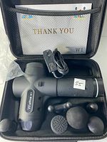 Open carrying case showing massage gun, charger, multiple heads, booklet