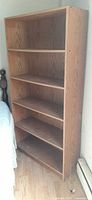 Full view of 5-shelf woodgrain bookcase beside bed