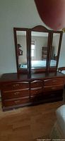 Front view of dark wood dresser with attached triple mirror, showing drawer arrangement and hardware