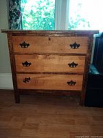 Front view showing three drawers, wood tones and metal pulls