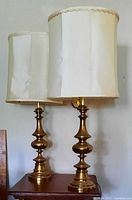 Two matching brass table lamps with off-white drum shades on side table