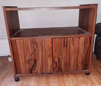Front view of woodgrain TV stand showing open shelf, two-door cabinet and casters