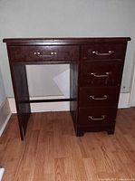 Front view of dark brown wooden writing desk with five drawers and brass-tone handles