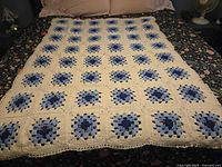 Full view of cream throw with blue granny squares spread on bed