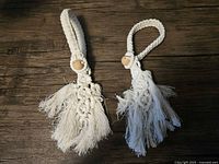 Front view of the two off-white macrame curtain tiebacks with wooden beads and fringe