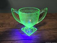 Front view of green depression glass sugar bowl glowing under UV light