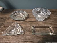 Four clear glass ashtrays on table: round pressed, round footed, triangular, rectangular