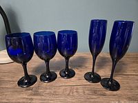 Front view of three wine goblets and two champagne flutes in cobalt blue glass