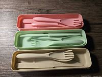 Three pastel cutlery sets in open cases displaying utensils