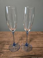 Two clear champagne flutes with pale blue stems standing side by side on wood surface