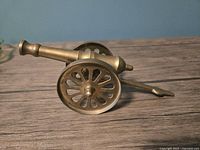 Side view of brass miniature cannon showing barrel and wheels