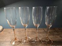 Four clear glass champagne flutes with pink stems standing side by side