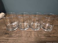 Four clear lowball glasses with gold plaid pattern lined up side-by-side