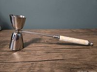 Full view of cocktail jigger standing upright, showing both metal cups and handle