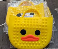 Two yellow duck pop-it purses, one atop another, packaged in plastic