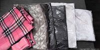 Group of scarves showing pink plaid pair and pashmina scarves in brown, black, and white within plastic