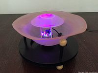 Overall view of glass bowl fountain on black base, illuminated purple