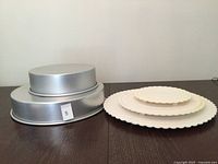 Stacked round aluminum cake pans beside stacked white plastic scalloped plates